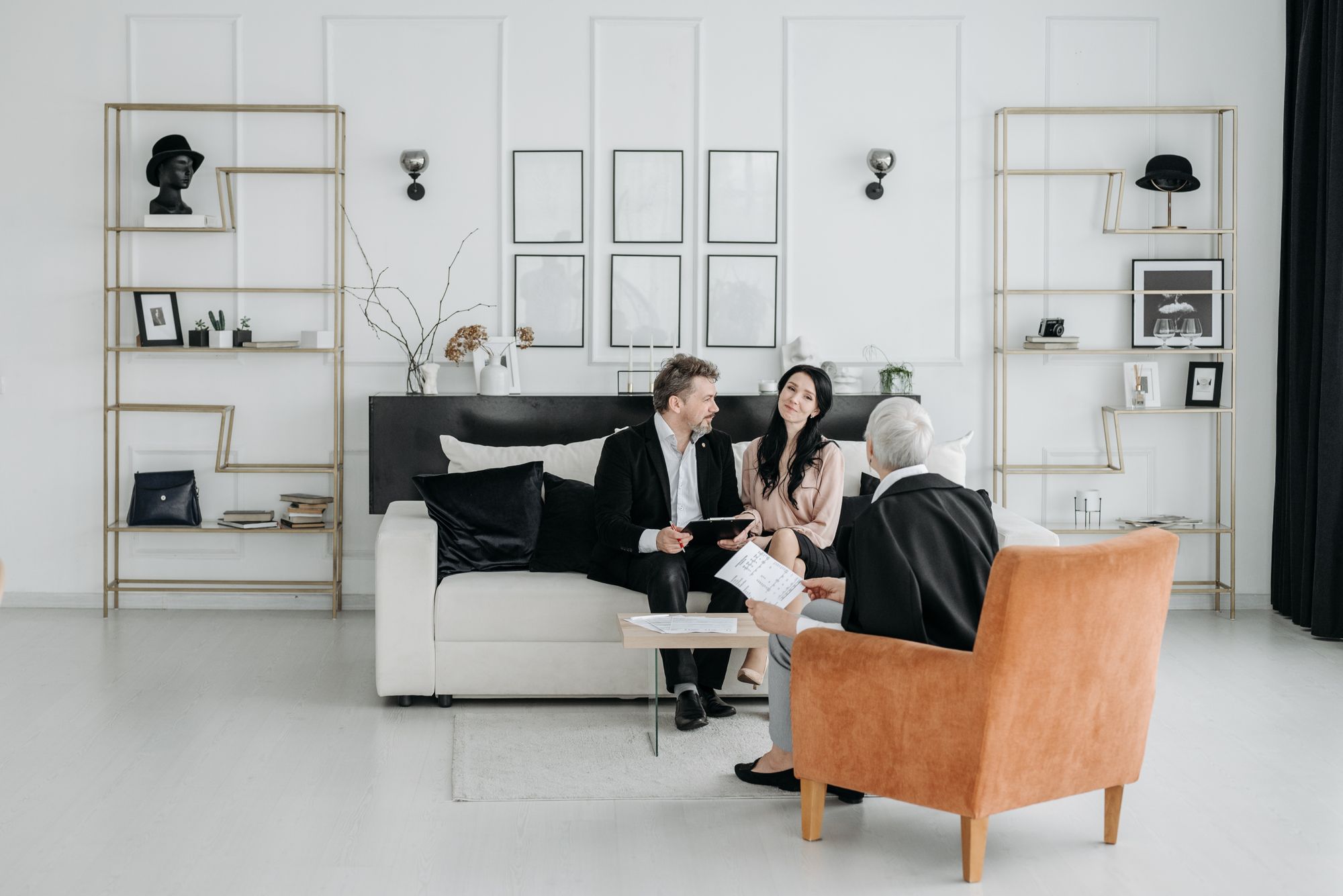 Trois personnes échangent dans un bureau élégant, canapé blanc, fauteuil cognac et étagères dorées