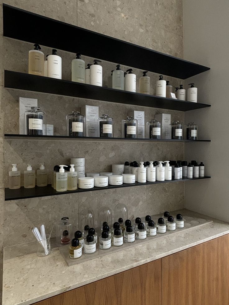 Rayonnage d’une boutique de parfums et de soins : mur de pierre, étagères noires, flacons et pots